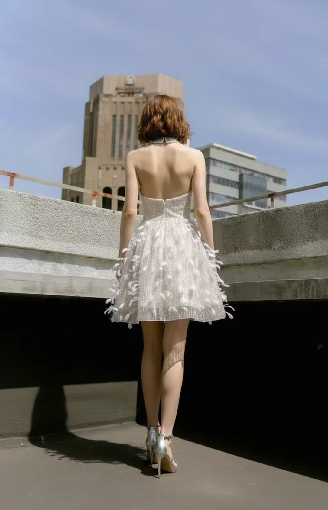 Back view of a short white halter neck feather cocktail dress with an open back