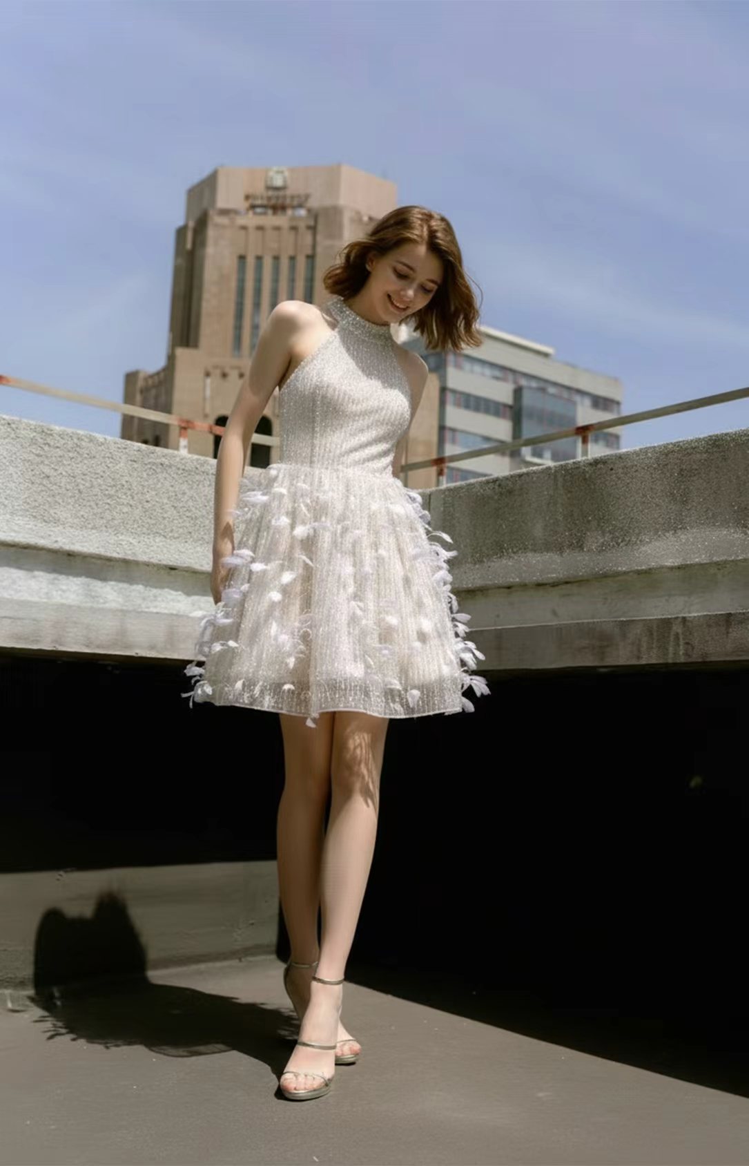 Model wearing a short white halter neck feather cocktail dress in an urban setting