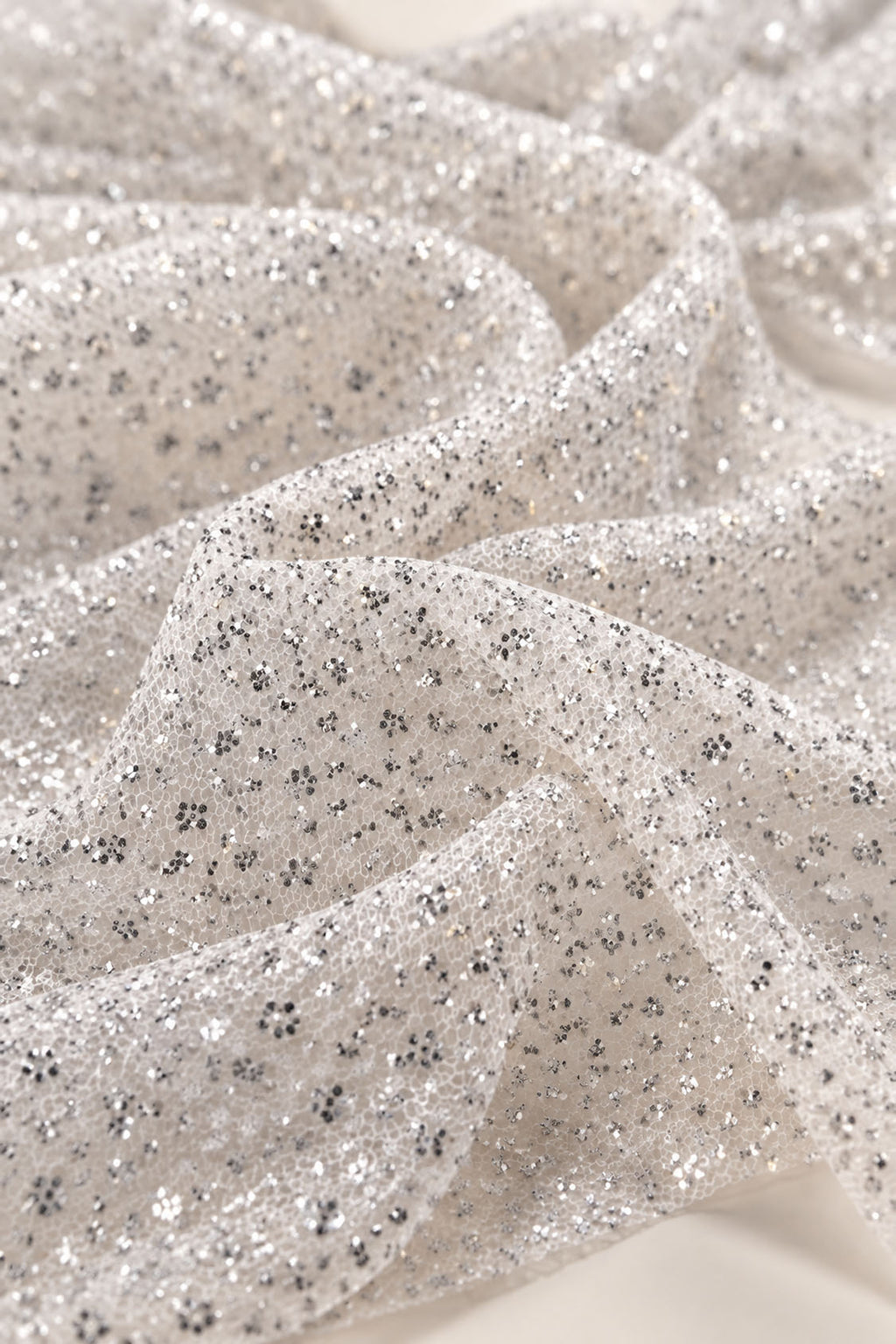 Close-up of silver glitter tulle mesh fabric with bonded glitter clusters used for a ball gown prom dress, crystal-like sparkle