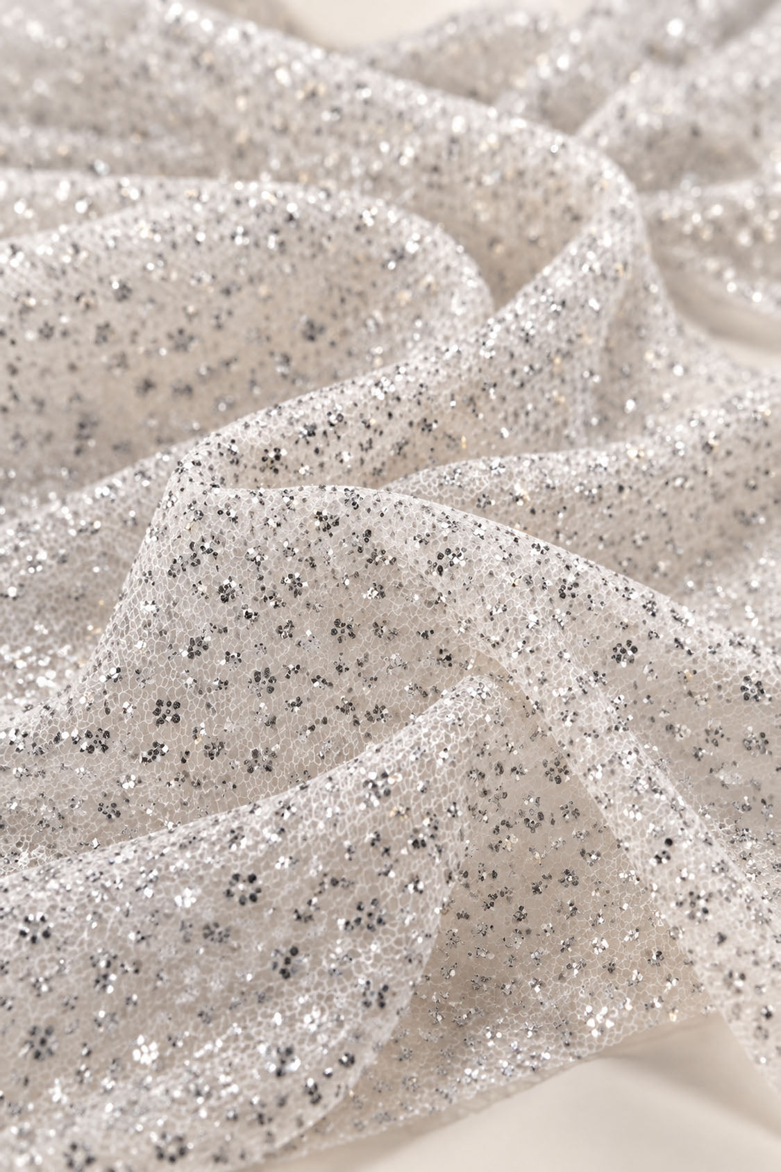Close-up of silver glitter tulle mesh fabric with bonded glitter clusters used for a ball gown prom dress, crystal-like sparkle